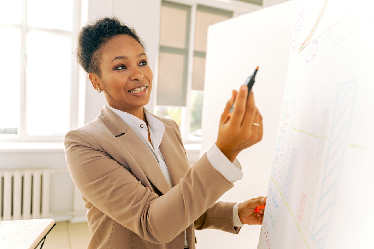 Formatrice souriante animant une formation d'anglais professionnel au tableau en entreprise