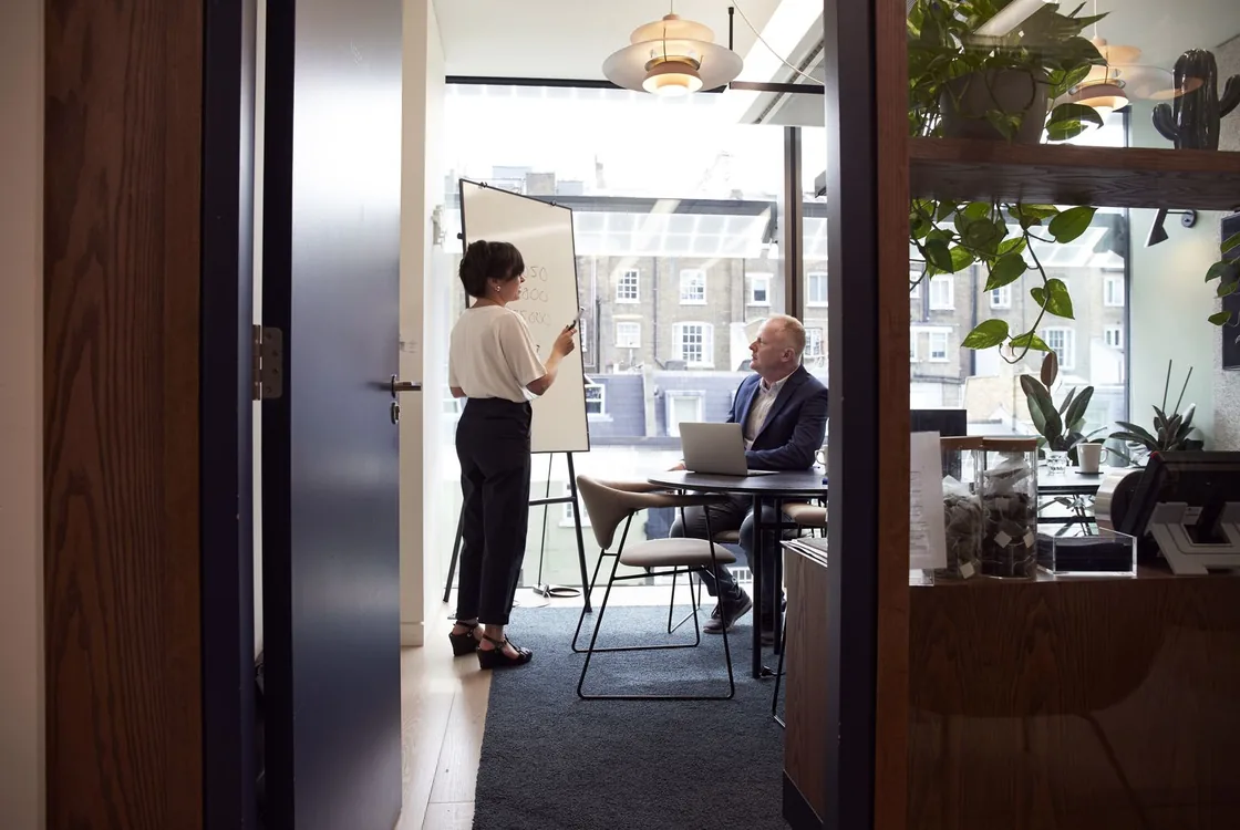 Commerciale animant un pitch devant un client en salle de reunion, anglais de la prospection